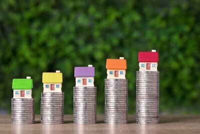 Five toy houses sitting on piles of coins