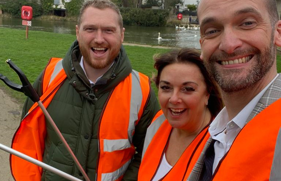 Three people posing in hi-vis jackets with a litter picker