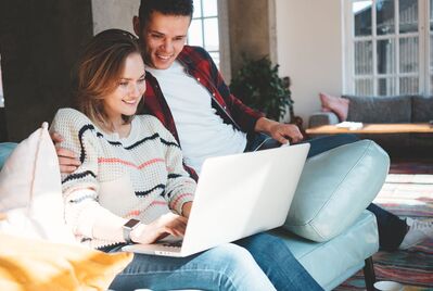 Two people sitting on a sofa together in front of a laptop