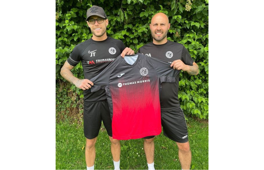 Two people holding up a football t-shirt with the Thomas Morris sponsorship 