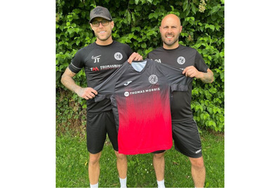 Two people holding up a football t-shirt with the Thomas Morris sponsorship 