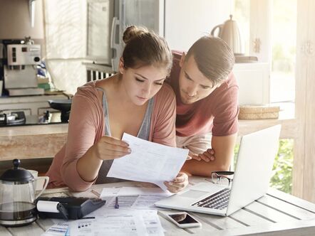 Two people looking at a sheet of paper in front of a laptop