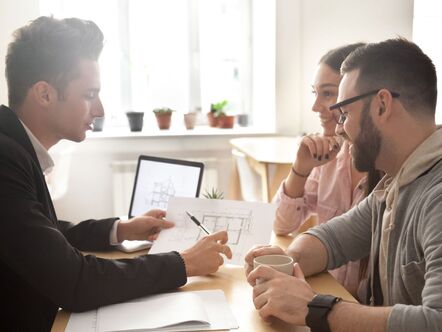 Two people sitting with an estate agent showing them a bueprint of a house